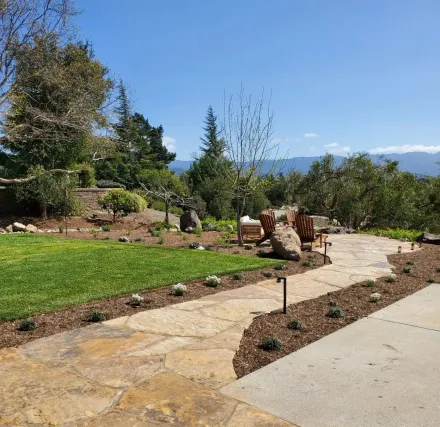 A stone walkway leading to a lush green field with mountains in the background.
