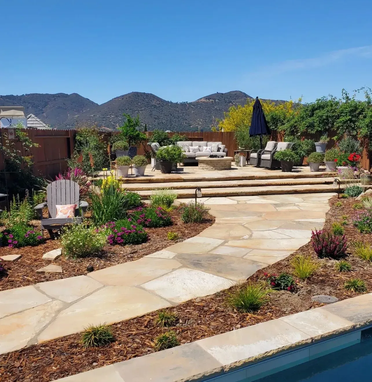 A stone walkway leading to a swimming pool with mountains in the background