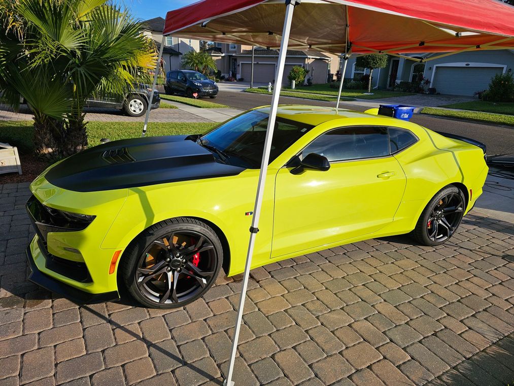 Bright yellow sports car with black hood parked in a driveway under a red canopy