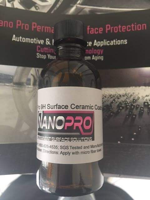 Bottle of NanoPro automotive ceramic coating on a promotional signboard background