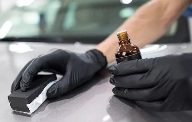 Gloved hands applying car polish to a silver vehicle with an applicator and bottle