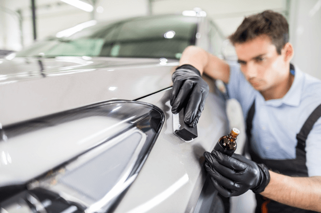 Mechanic polishing a silver car’s front fender in an auto shop