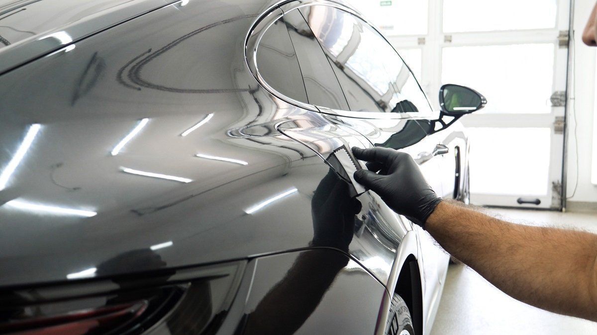 Person polishing a gray sports car with a cloth in a garage