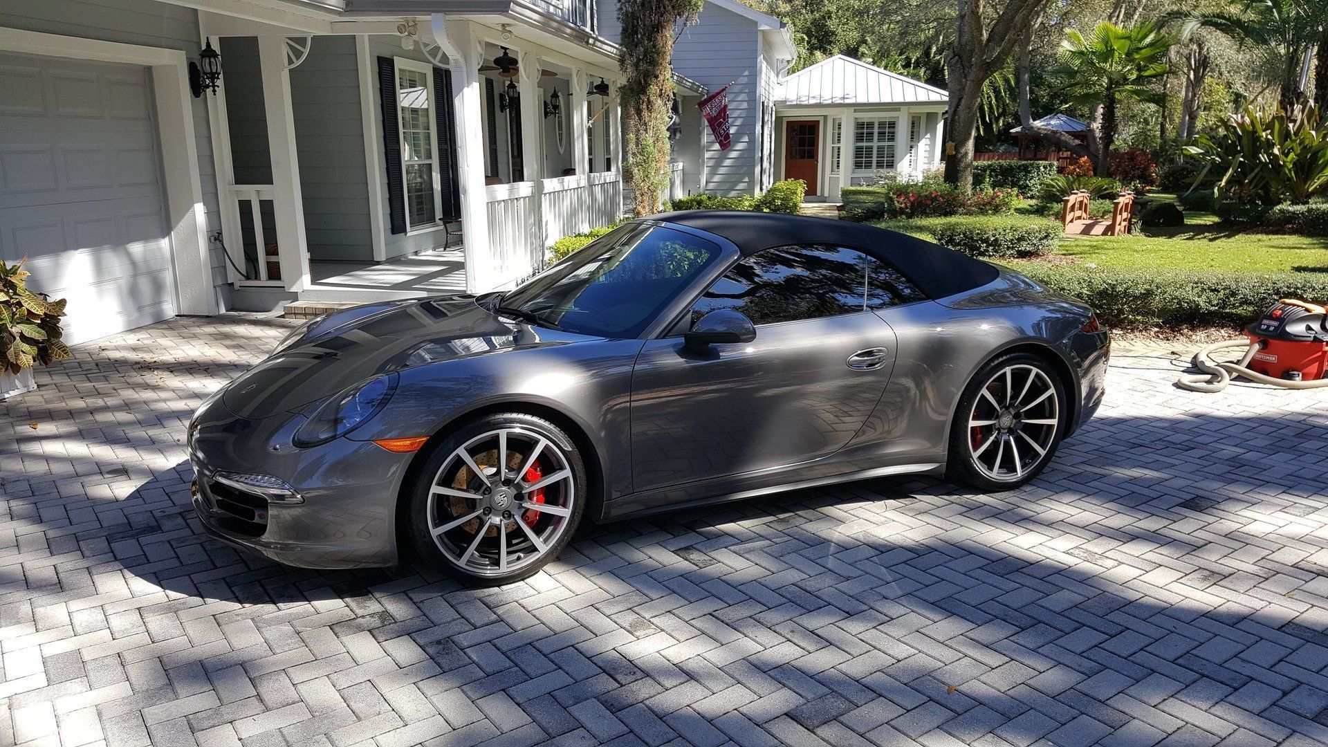 Black sports car parked in a driveway beside a house on a sunny day