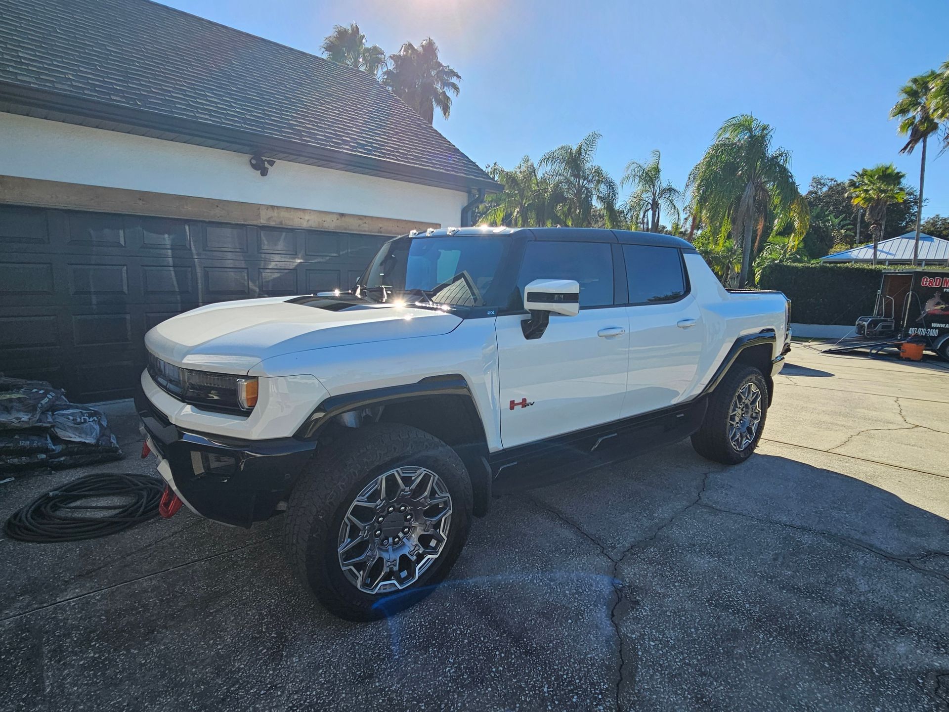 White lifted pickup truck parked in a sunny driveway beside a house