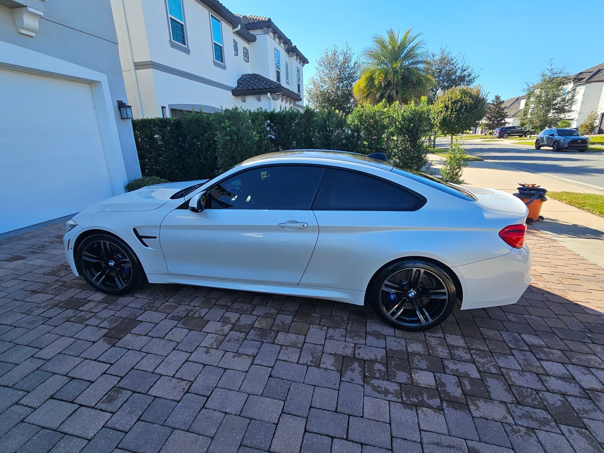 White coupe parked in a driveway beside a house, with tinted windows and black wheels.