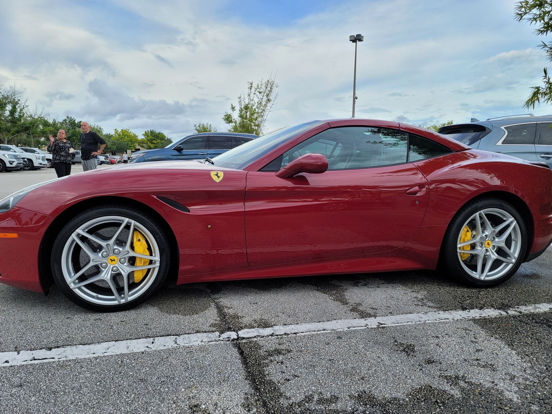 Red Ferrari sports car parked in a lot under a cloudy sky, side view.