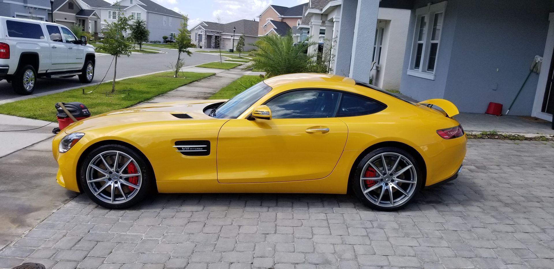 Yellow sports car parked in a driveway outside a suburban house, side view