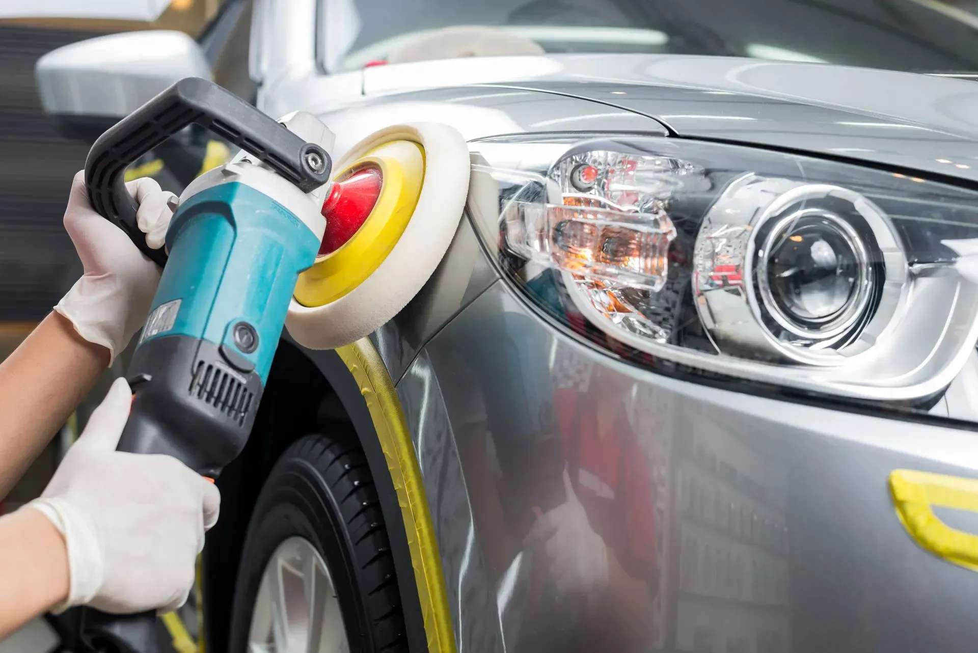 Car polisher buffing a silver car’s headlight and front fender with a rotary tool