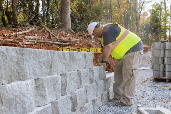Construction worker in safety vest using a level on a gray  concrete retaining wall. Outdoor setting.