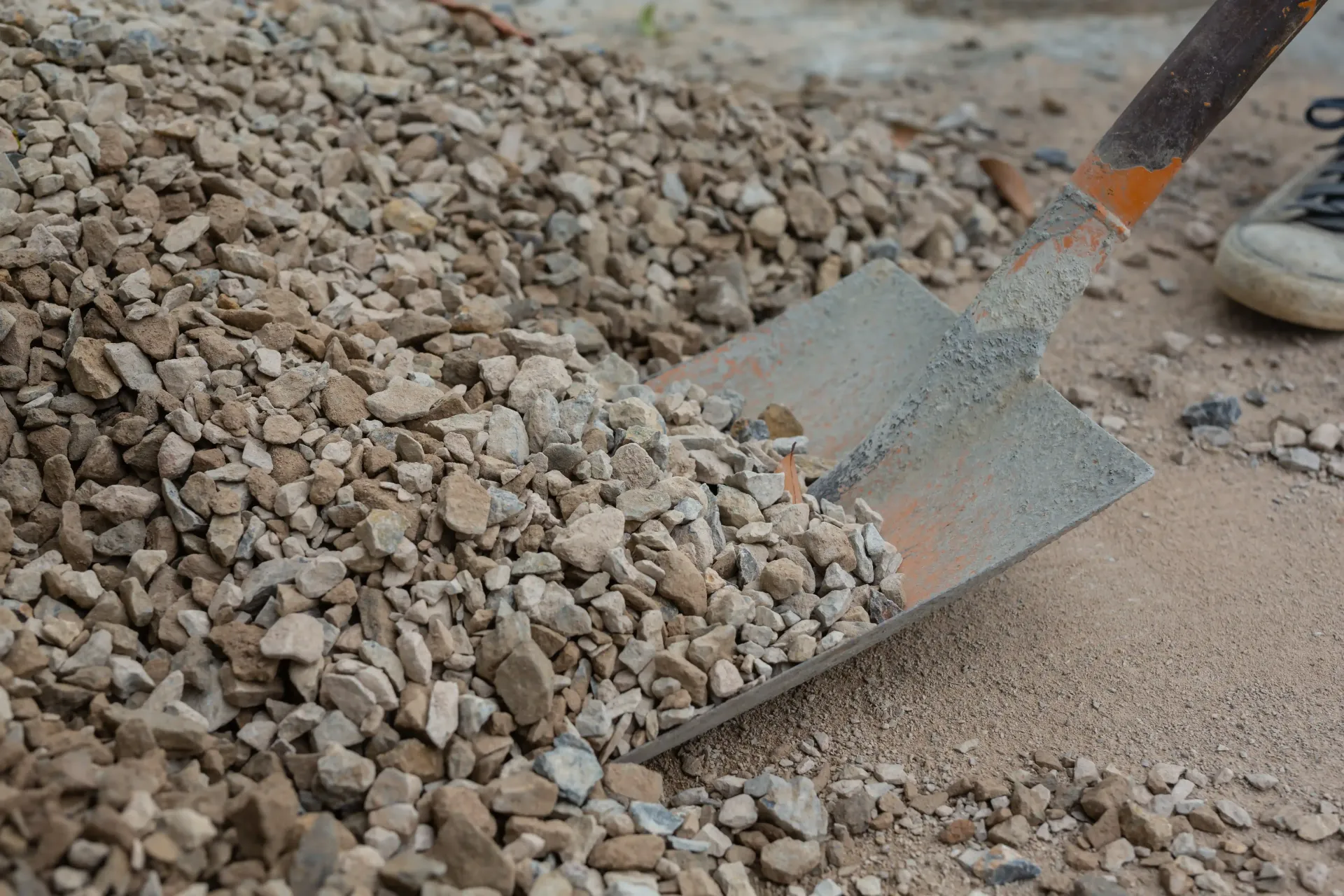 Pile of gravel being scooped with a rusty shovel; close-up shot.
