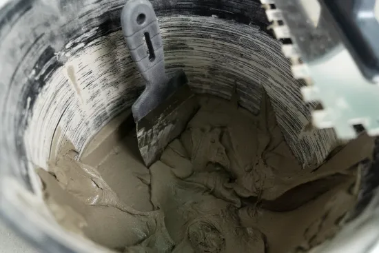 Gray mortar in a bucket, with a notched trowel resting in it.