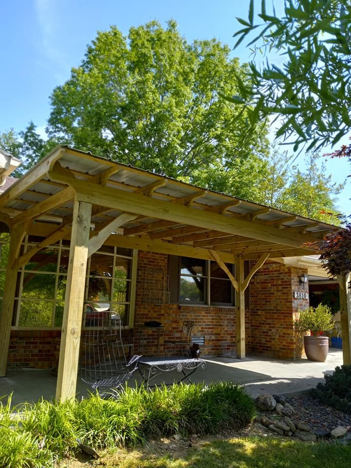 Wooden porch cover over a brick building, with a tree in the background on a sunny day.
