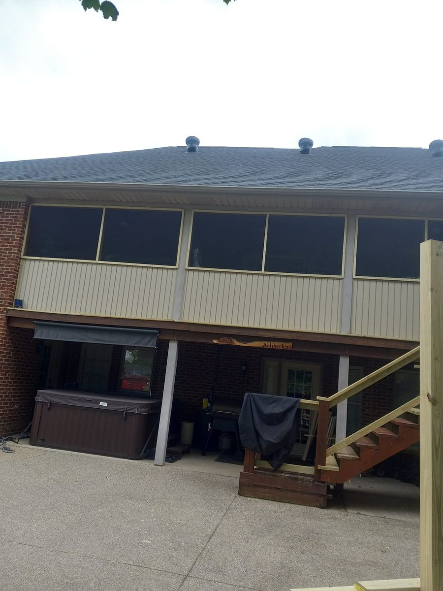 Backyard deck with hot tub under a screened-in porch attached to a brick house.
