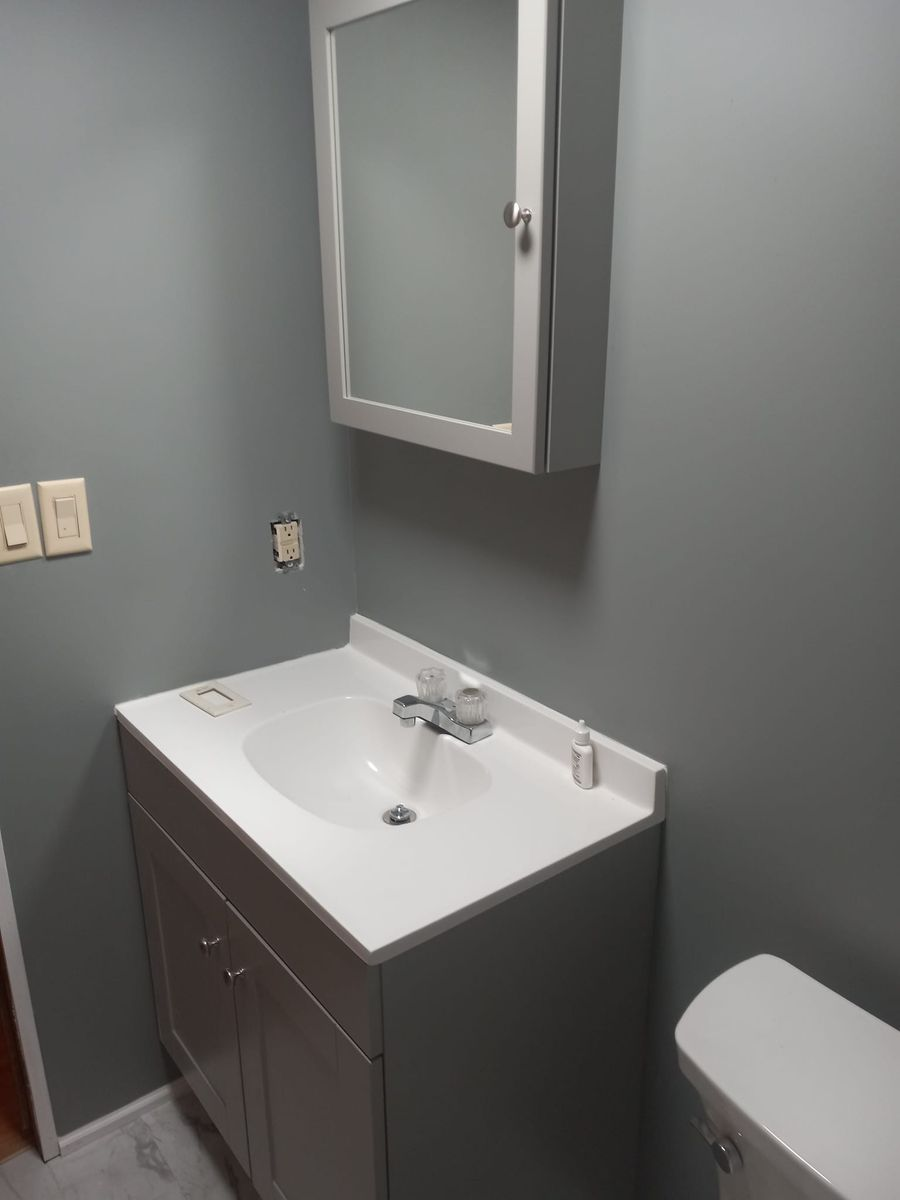 Gray-walled bathroom with white sink, cabinet, and mirror. Toilet to the right.