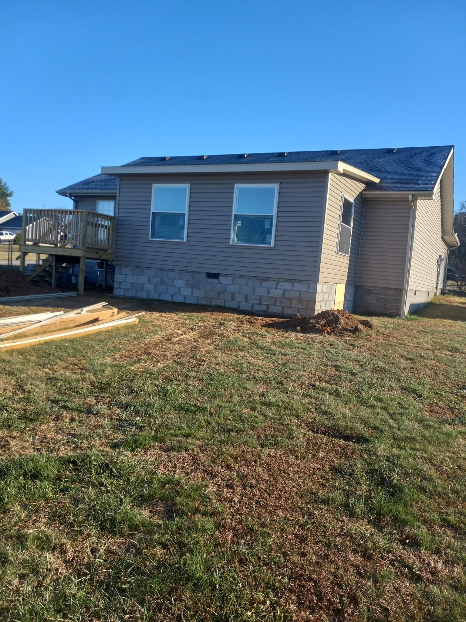 Small house under construction, gray siding, blue roof, with a wooden deck, and clear blue sky.