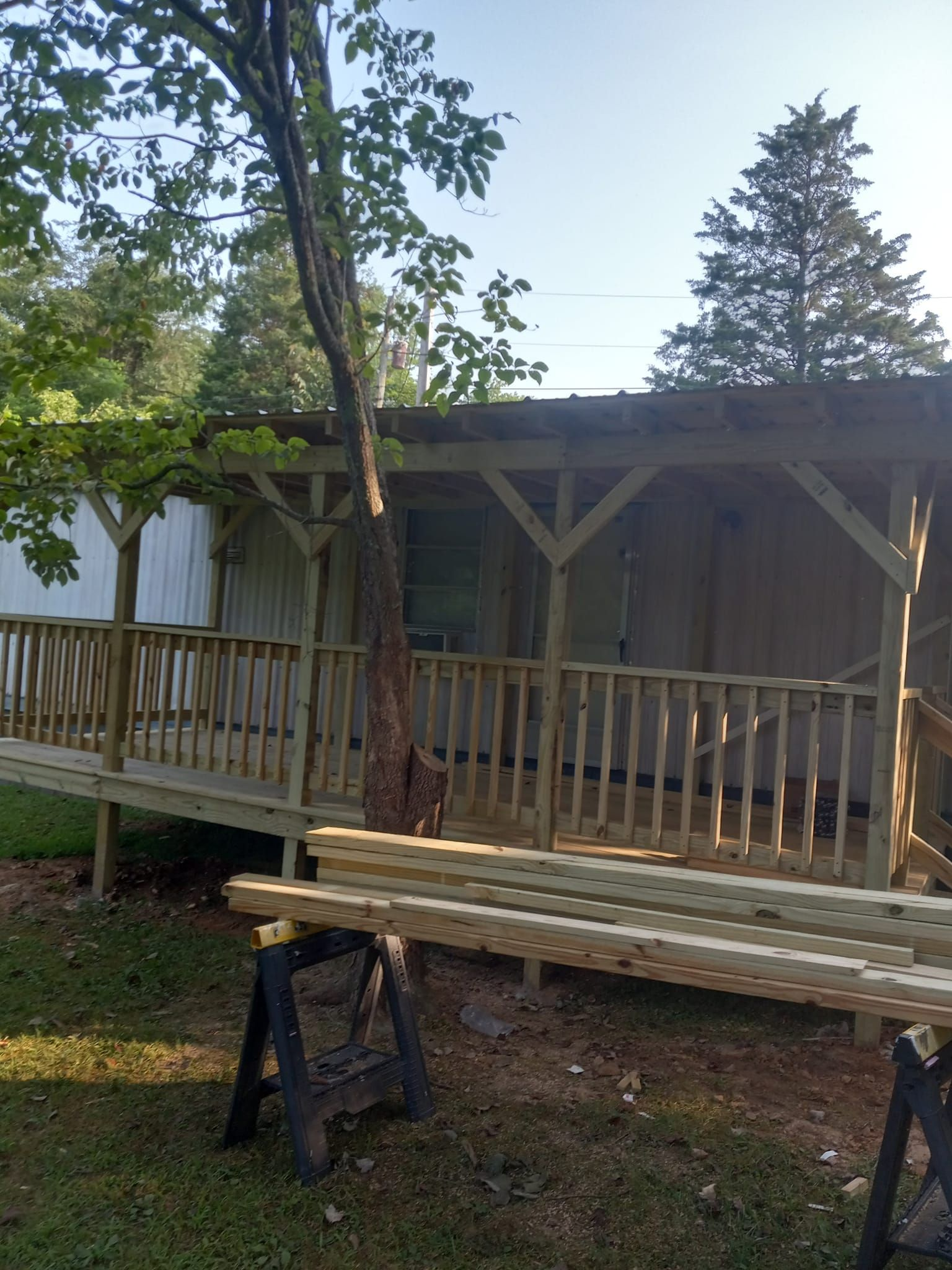 A newly built wooden porch on a mobile home, with sawhorses holding lumber in foreground.