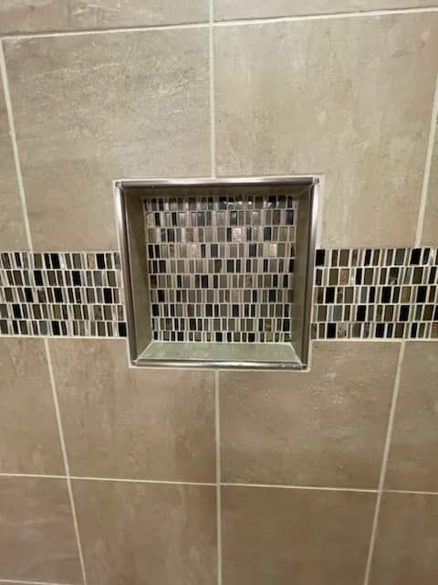 Tile shower niche with mosaic tile backing and decorative border.