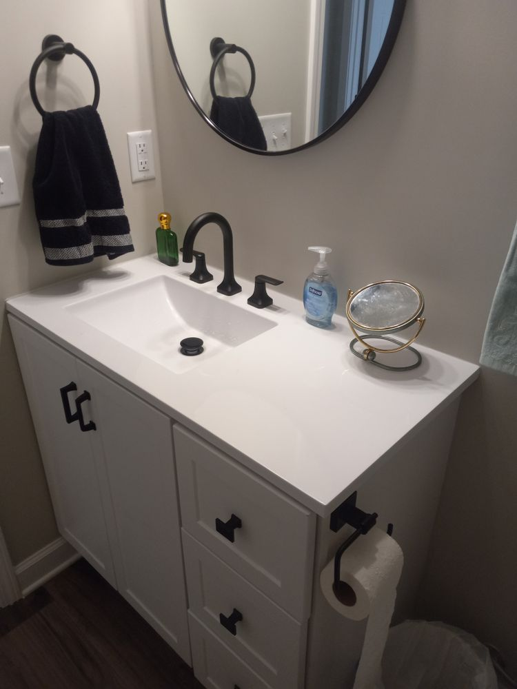 White vanity with black fixtures, round mirror, and black towel in a bathroom.