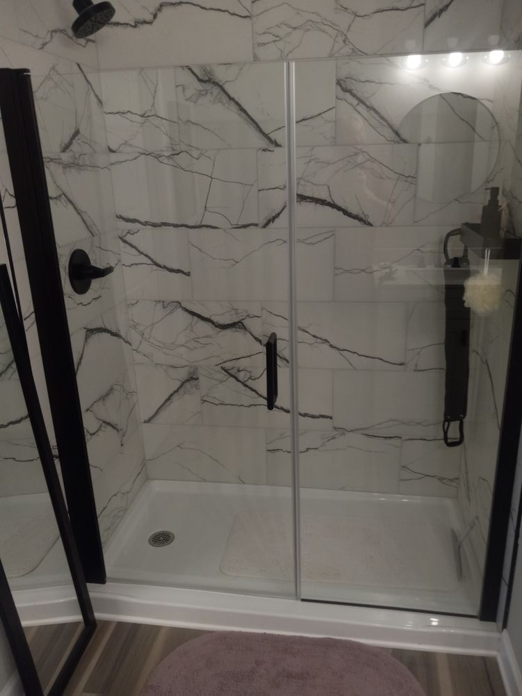 Modern shower with marble-look tile, black fixtures, and glass door.