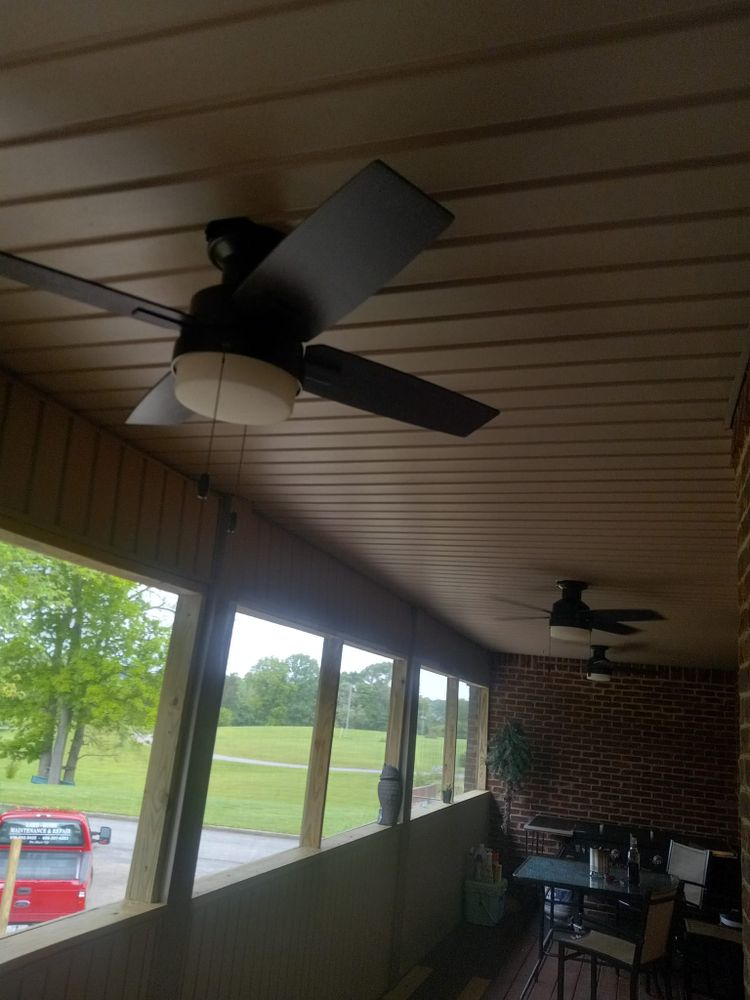 Two black ceiling fans with lights on a covered porch overlooking a grassy area.