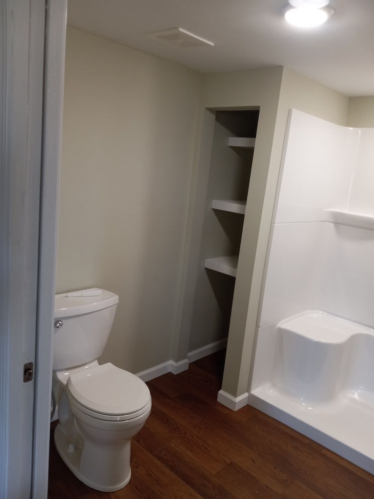Bathroom with toilet, shower, and built-in shelves. Walls are light beige, flooring is wood-look.