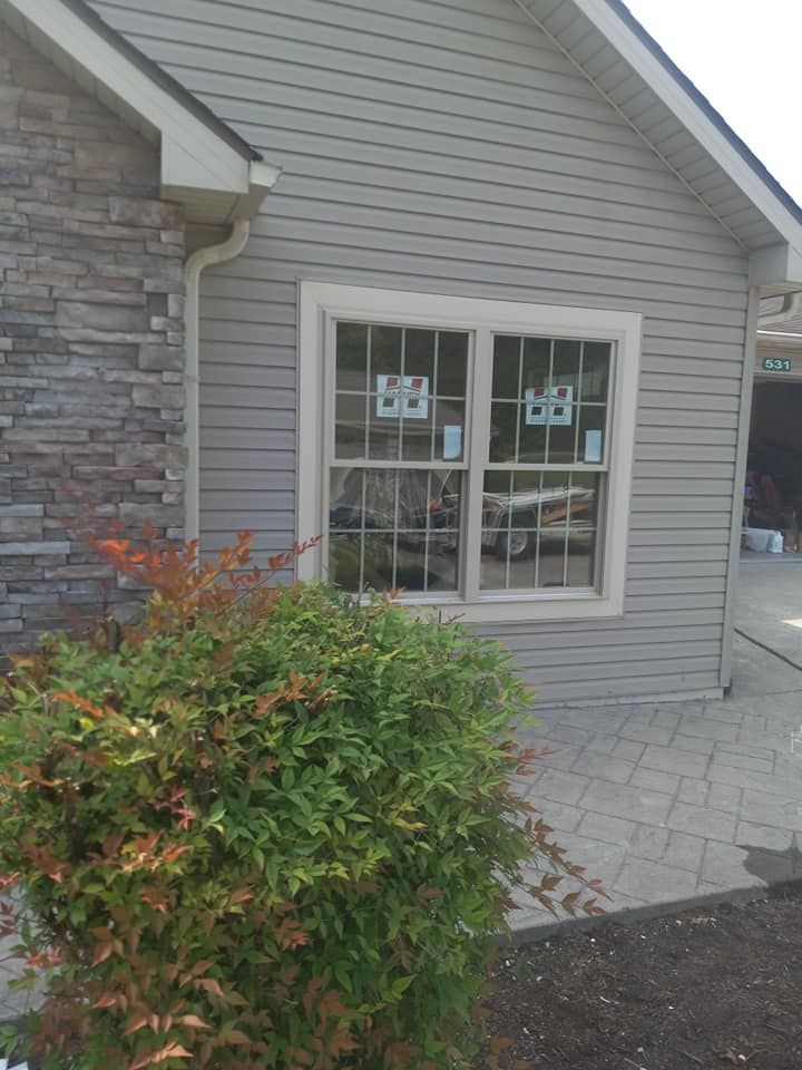 House exterior with light siding, stone facade, window, and green bush.