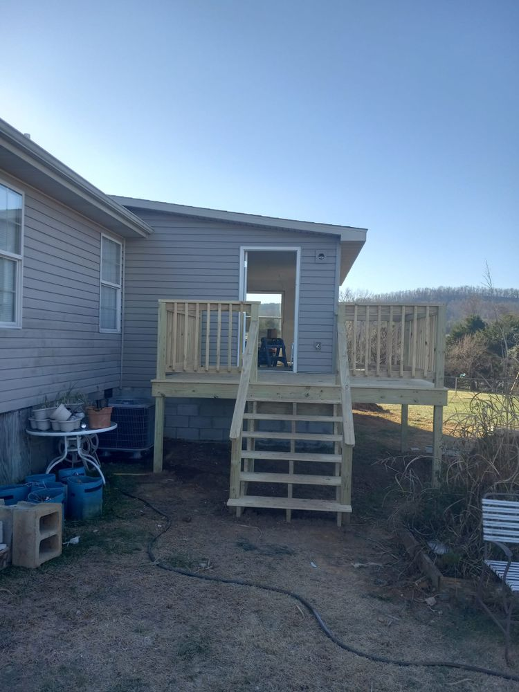 A wooden deck with steps attached to a gray house with a small shed.