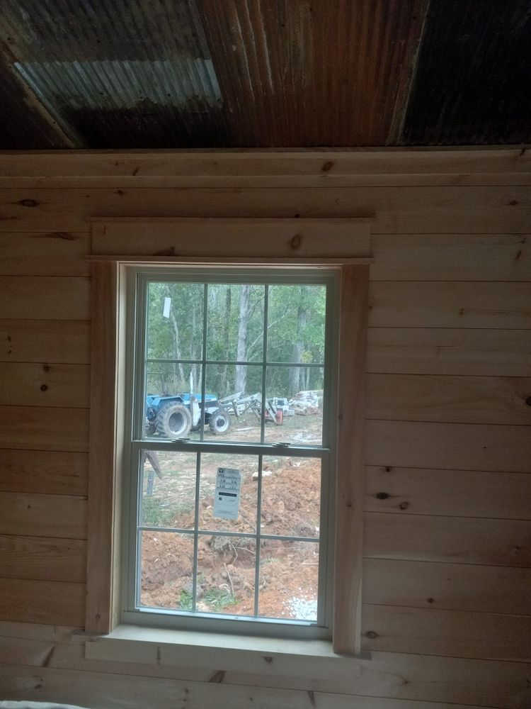 Window in a wooden-walled room, framed with light wood trim. Outside, a blue tractor is visible.