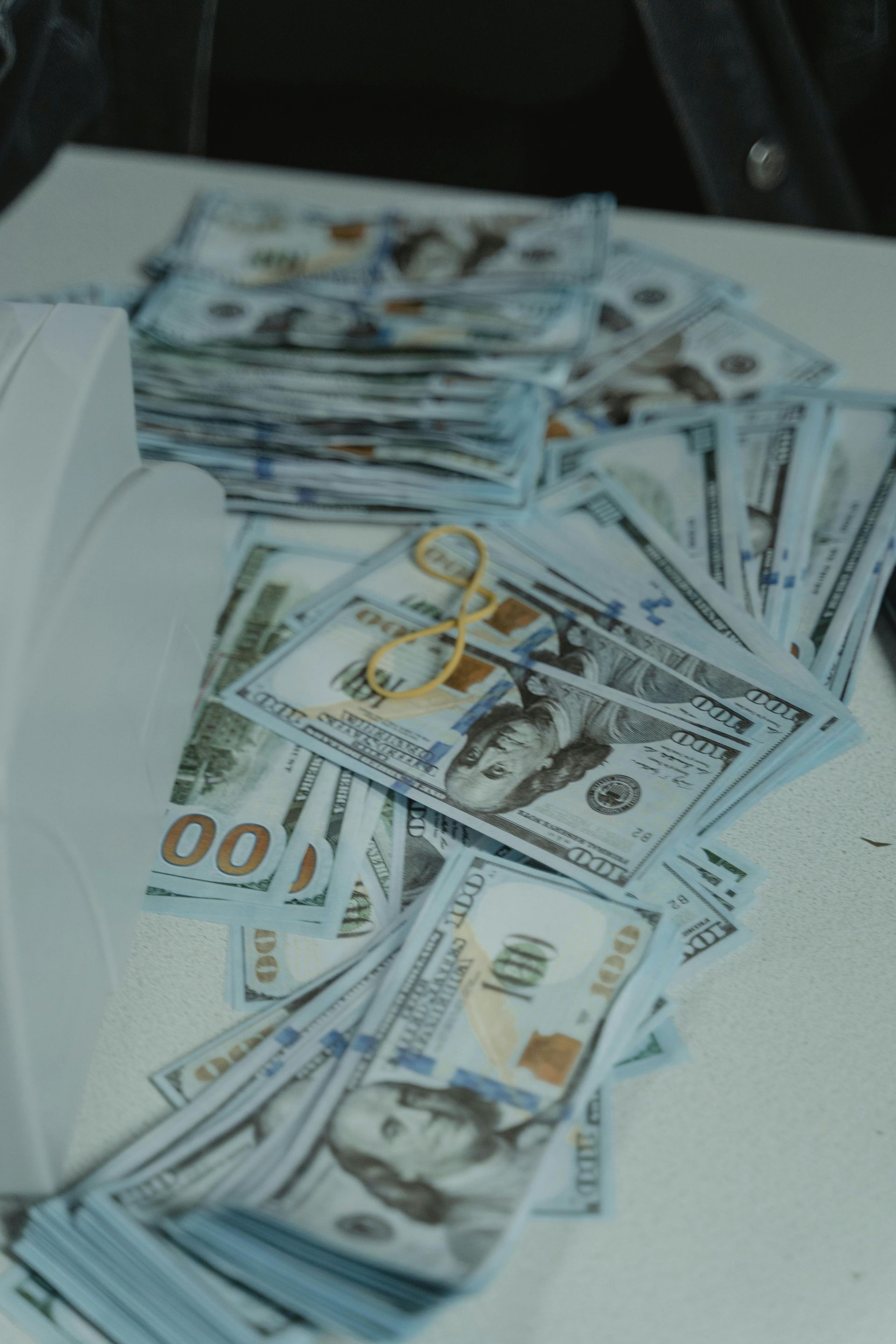 Scattered stacks of U.S. hundred-dollar bills on a white surface.
