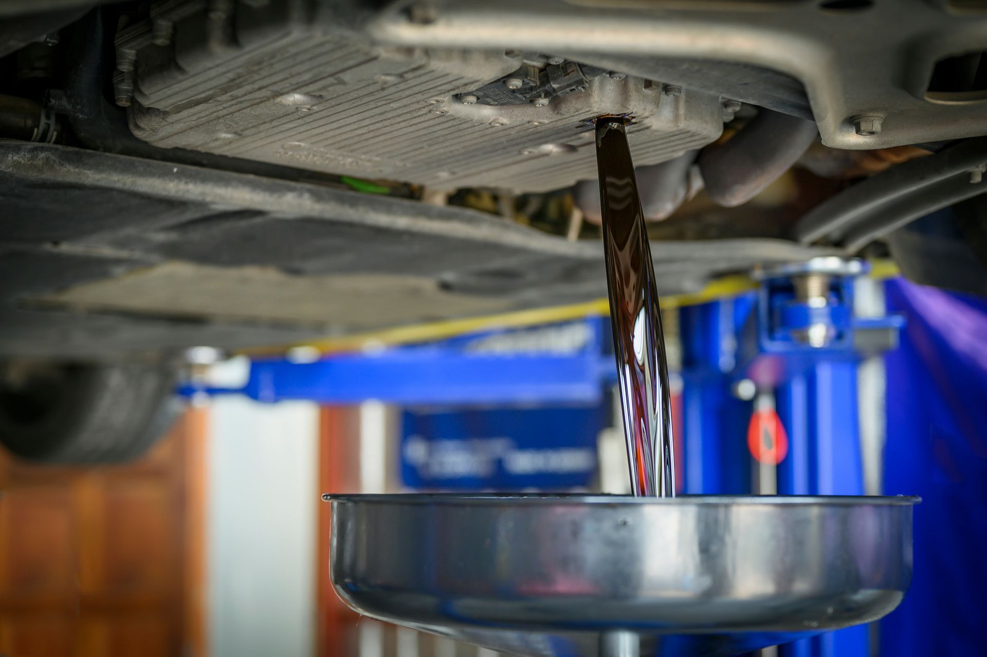 A Person Is Pouring Oil Into A Bucket Under A Car — Torque Tech Supply & Repairs In Port Macquarie, NSW