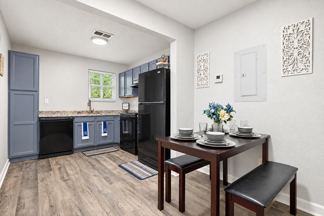Small modern kitchen with black appliances, gray cabinets, and a dining table with flowers.
