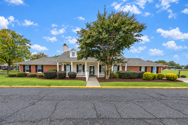 Single-story brick building with white columns, centered entrance, and trees under a blue sky