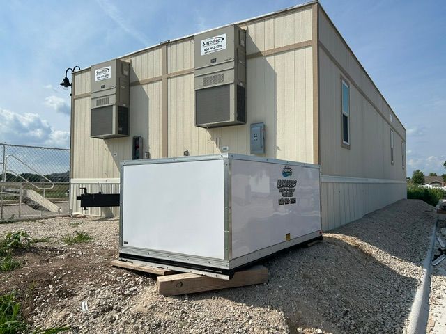 White portable generator unit outside a beige modular building on gravel.