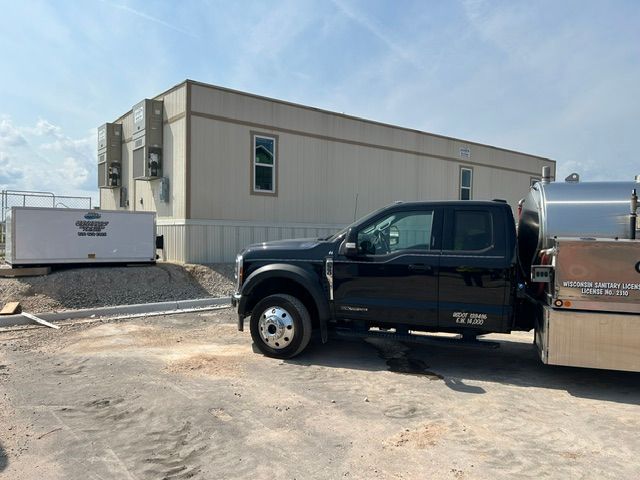 Black pickup truck and silver trailer parked beside a beige industrial building on a gravel lot