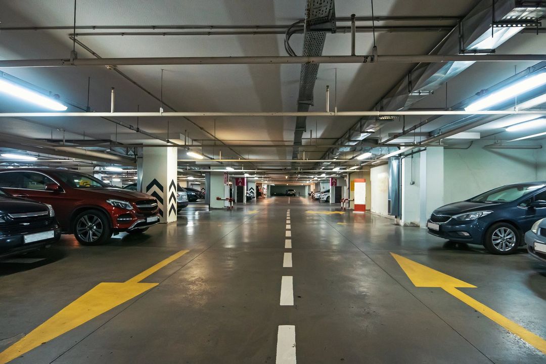 Corsia di un parcheggio sotterraneo con auto parcheggiate su entrambi i lati e frecce direzionali gialle sul pavimento
