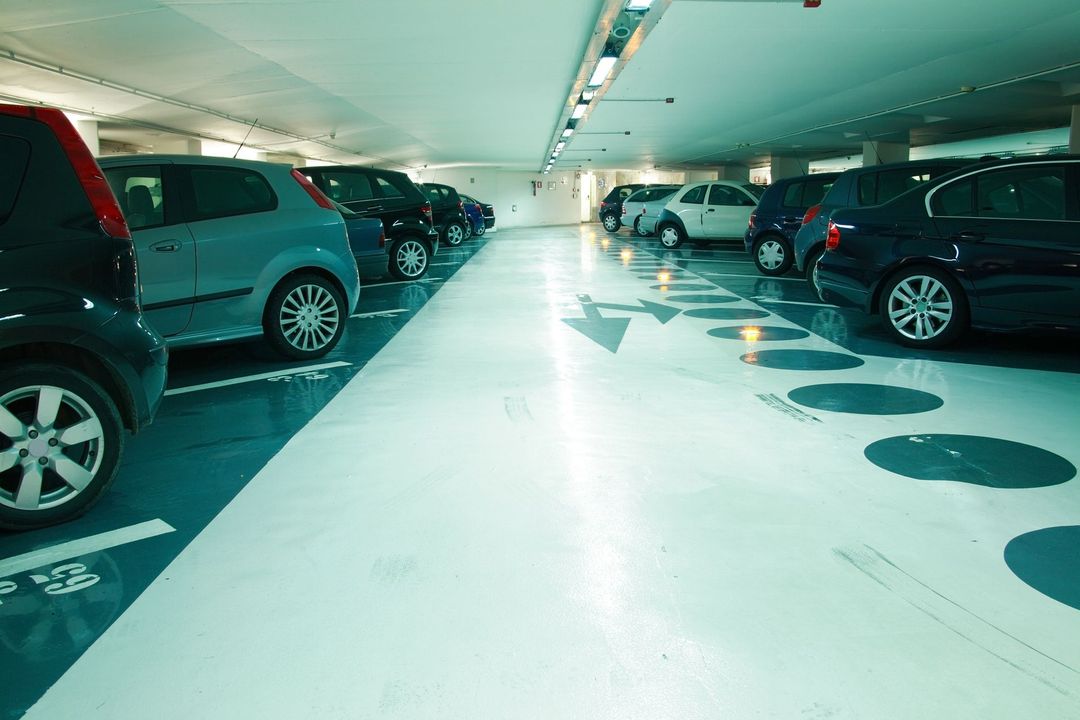 Parcheggio sotterraneo ben illuminato, con auto parcheggiate su entrambi i lati e una corsia centrale bianca con frecce.