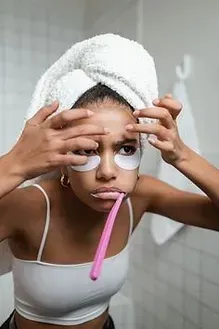 A woman with a towel wrapped around her head is brushing her teeth in front of a mirror
