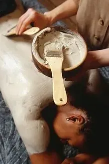 A woman is getting a massage with a bowl of clay on her back