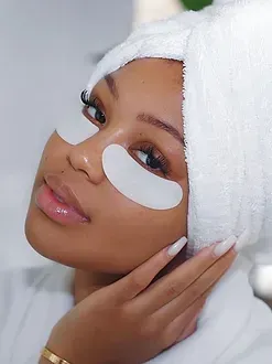 A woman with a towel wrapped around her head is wearing eye patches