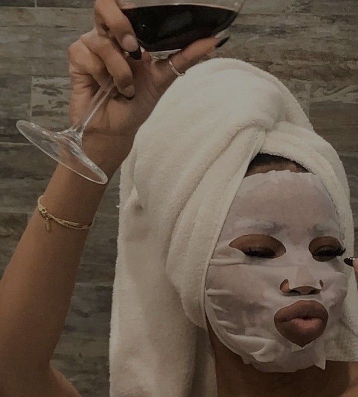 A woman with a mask on her face is holding a glass of wine.