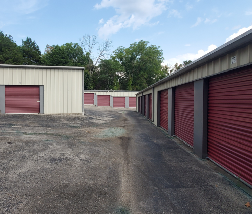Storage units with red doors in a paved lot under a partly cloudy sky.