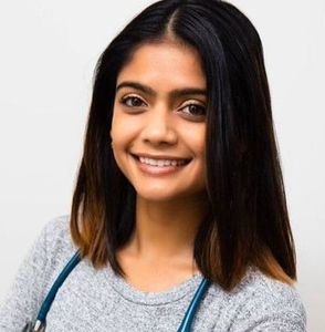 Woman with dark hair smiles, stethoscope around neck.