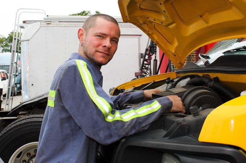 Andrew from Wallington Truck Repair performing diesel engine maintenance on a yellow truck in Wallington, NJ