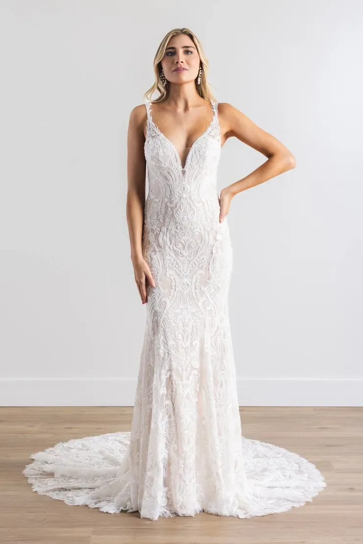 A woman in a white lace wedding dress is standing on a wooden floor.