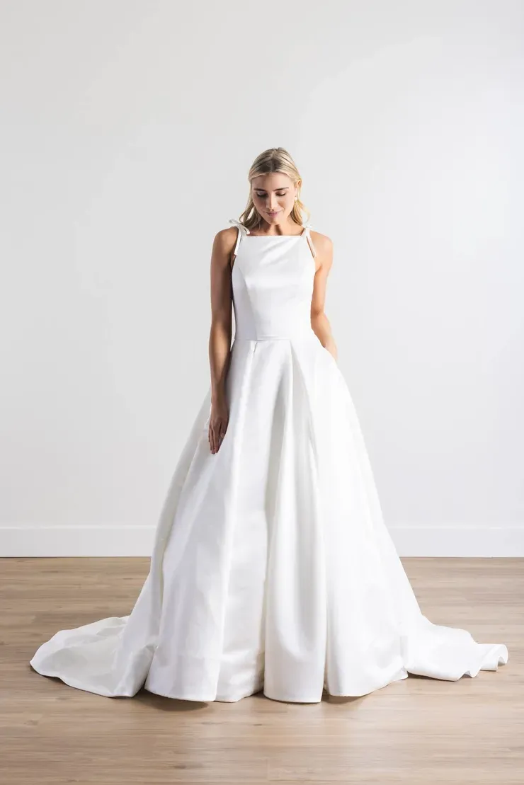 A woman in a white wedding dress is standing on a wooden floor.