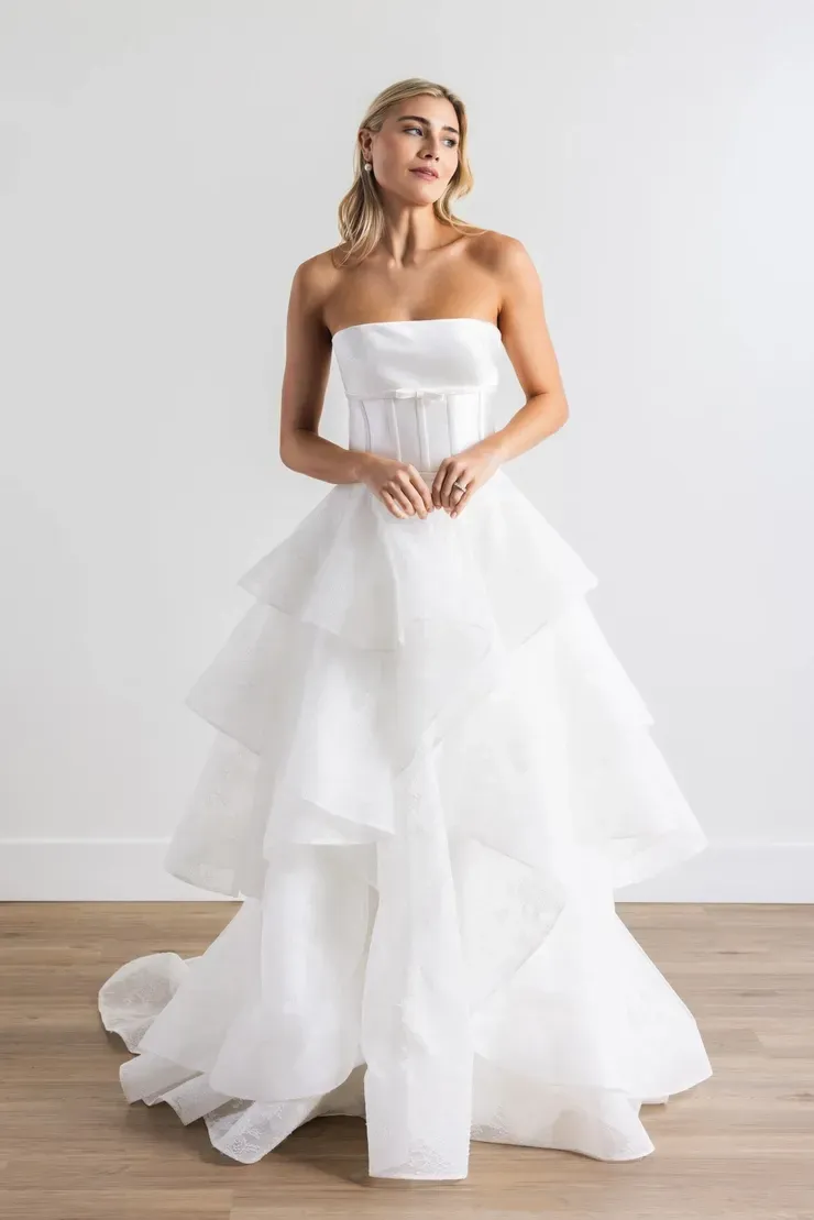 A woman in a white wedding dress is standing on a wooden floor.
