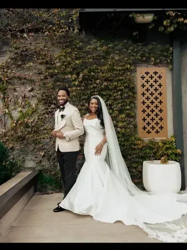 A bride and groom are standing next to each other in front of a wall.