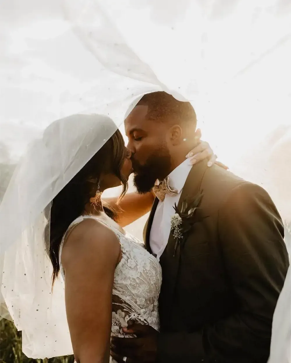 A bride and groom are kissing under a veil.