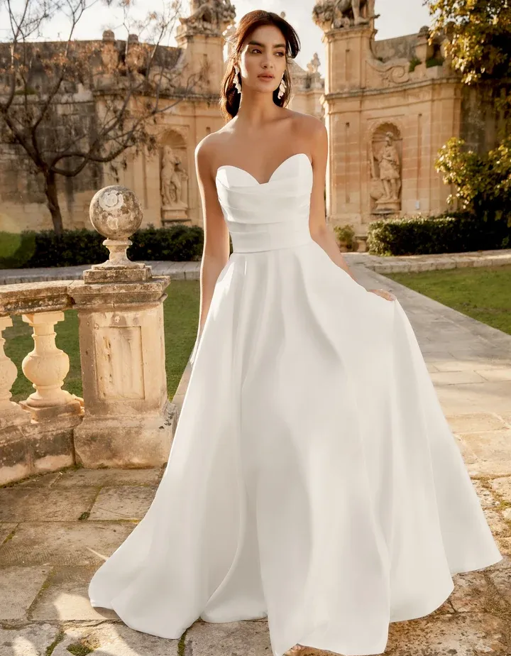 A woman in a white dress is standing in front of a building.